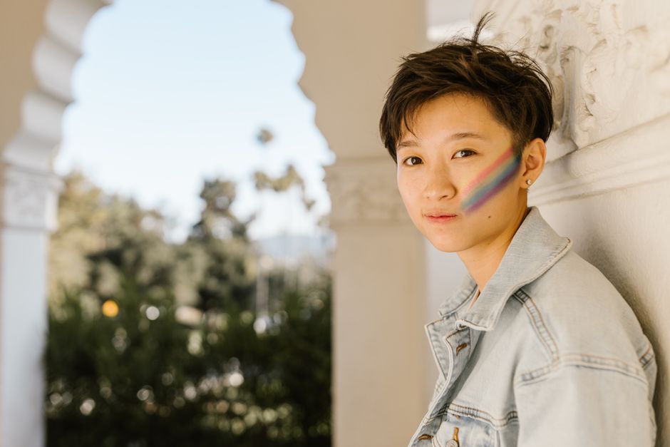 Portrait of a woman with short hair and rainbow face paint in a sunlit outdoor location.