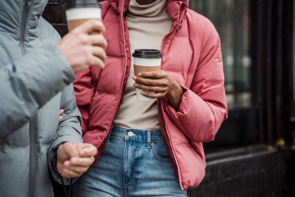 Unrecognizable couple in warm outerwear with tasty takeaway hot beverages standing on street near building on cold day in city