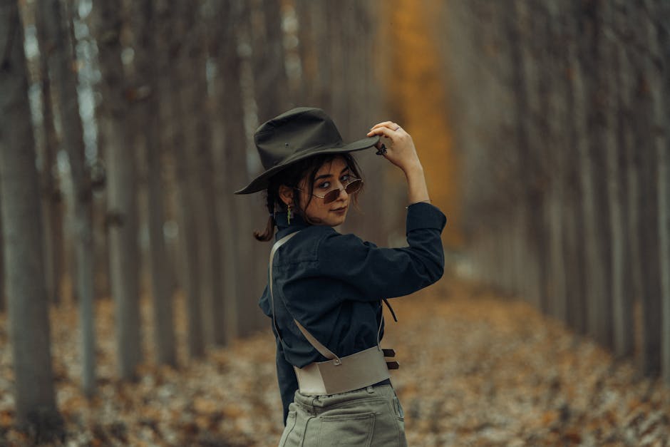 Woman standing in a forest wearing a hat and sunglasses in autumn.
