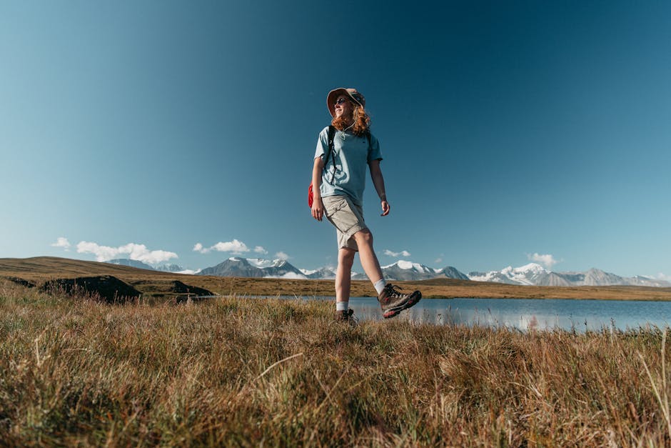 Woman enjoys a serene hike by mountains and river under a clear blue sky.