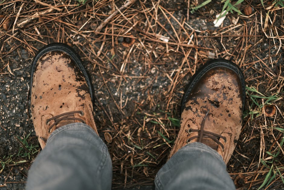 Close-up of rugged brown leather shoes stained with dirt on an outdoor surface.