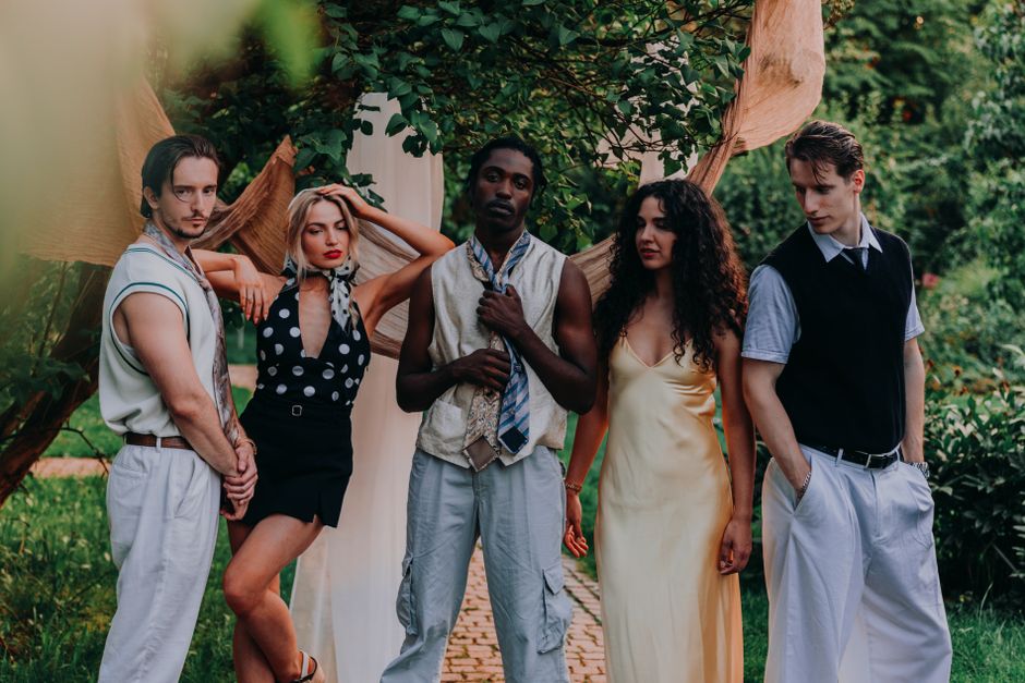 Five fashionable friends posing elegantly among lush garden greenery.