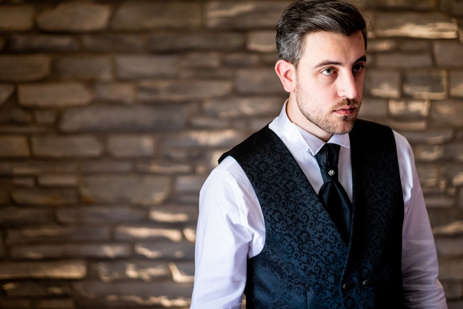 Stylish man in formal attire, posing against a stone wall, exuding elegance and charm.