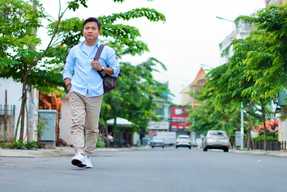 Man walking on a quiet city street on a sunny day with green trees.