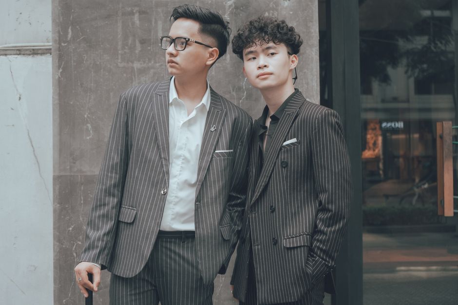 Two young men in striped suits pose stylishly outdoors in Hanoi.