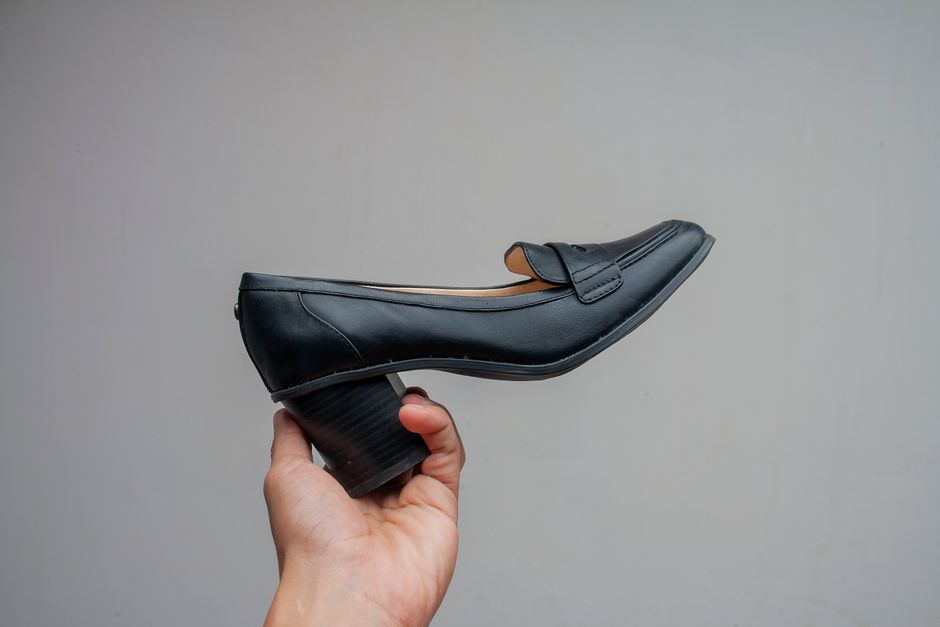 Black leather shoe held aloft by a hand, presenting elegant daytime style.