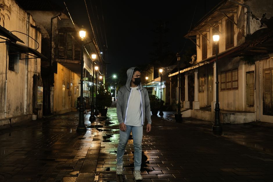 A young man in casual attire strolls through a historic street at night under warm streetlights.