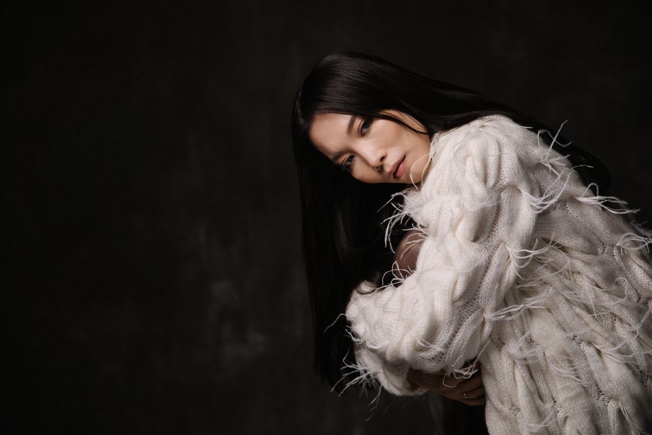 Stylish portrait of a woman wearing a textured white sweater in a dark setting.