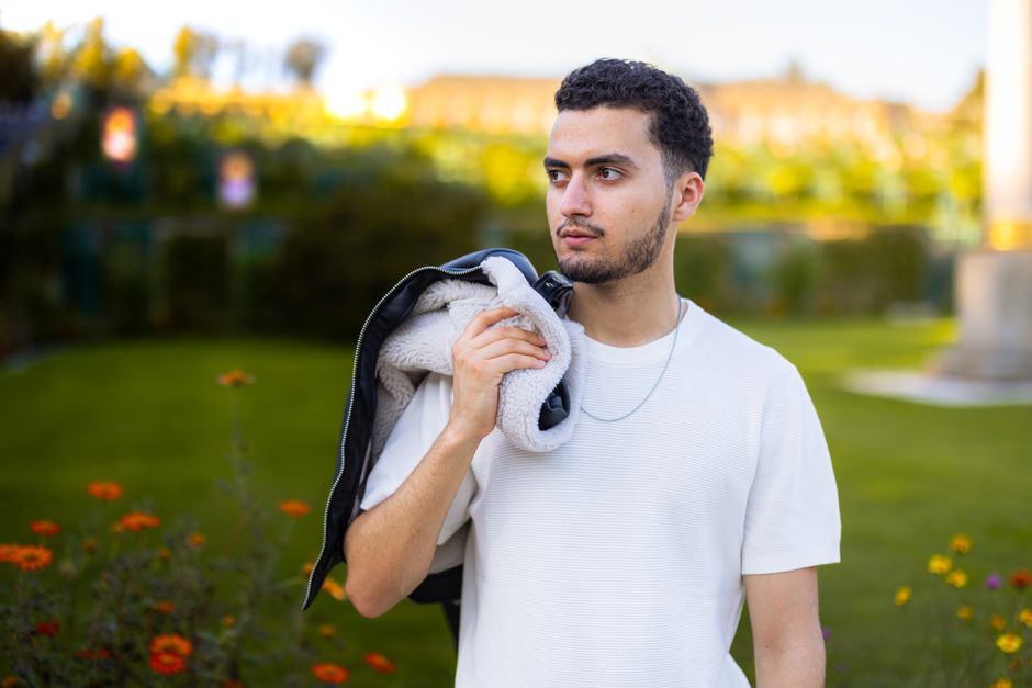 Portrait of a young man outdoors in a park holding a jacket over his shoulder.