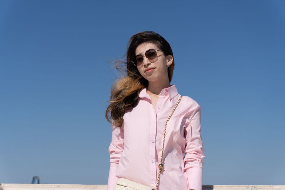 A fashionable woman in pink shirt and sunglasses standing against a clear blue sky.