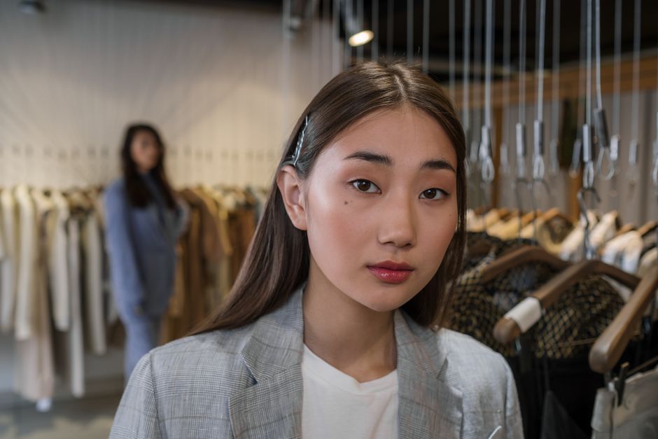 Close-up portrait of an Asian woman in a gray blazer, in a stylish fashion boutique with blurred background.