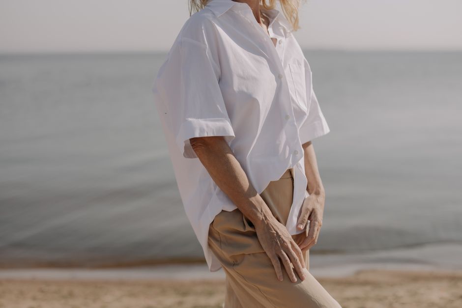 An elegant woman in a classic white shirt stands gracefully by the tranquil seaside.