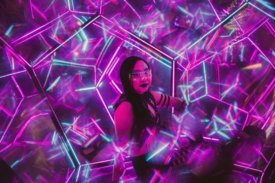 Futuristic portrait of a woman surrounded by neon lights and mirrors creating a kaleidoscope effect.