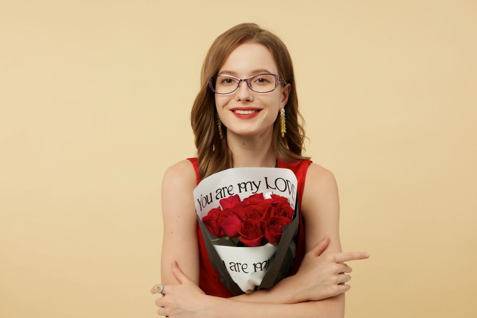 A smiling woman with glasses holding a bouquet of red roses, expressing love and joy.