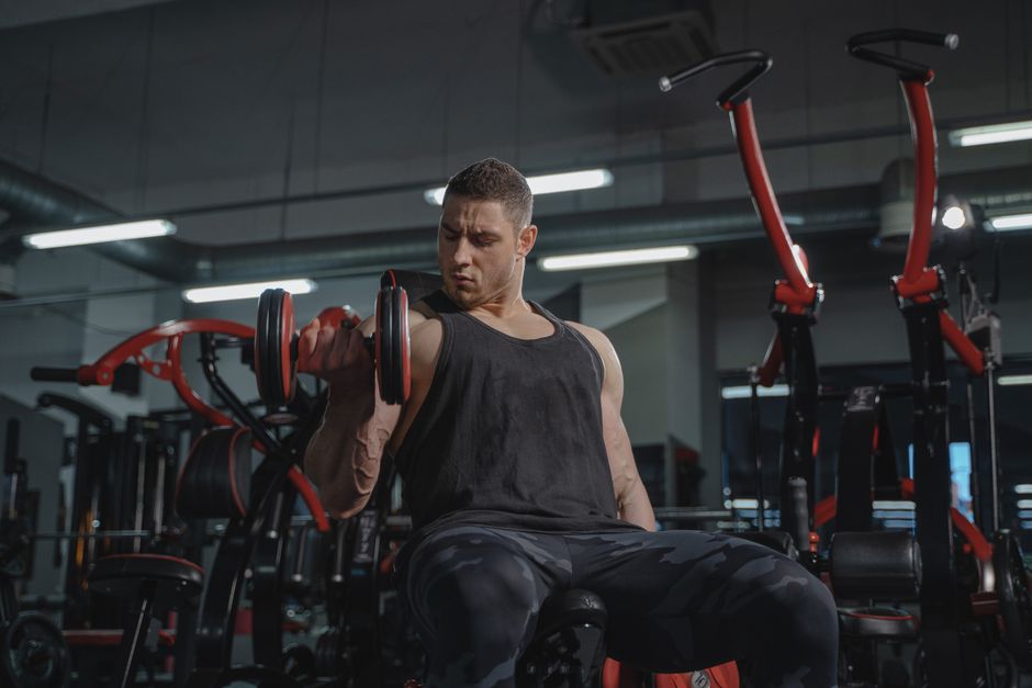 Athletic man performing dumbbell curls while sitting in a modern gym.