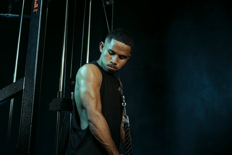 A man intensely exercising on a cable machine in a dark gym setting, highlighting fitness commitment.