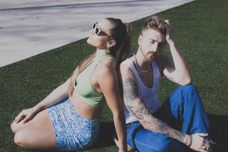 Stylish couple with tattoos and sunglasses enjoying summer relaxation on artificial grass.