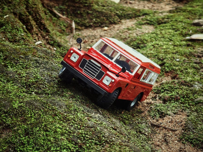 A realistic red diecast toy car climbing over lush green moss in an outdoor setting.