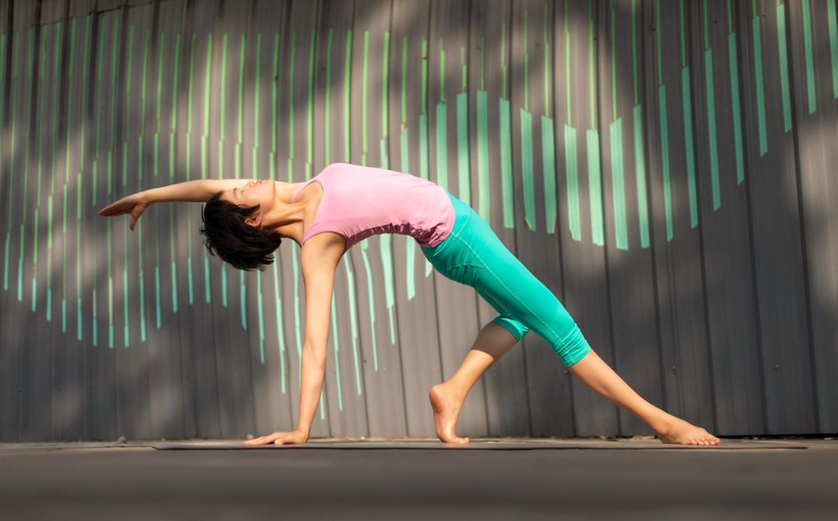 A woman performs a yoga pose outdoors, showcasing flexibility and grace in the daylight.