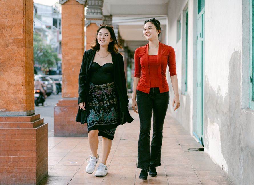 Two smiling women walk down an urban sidewalk, enjoying a sunny day in the city.