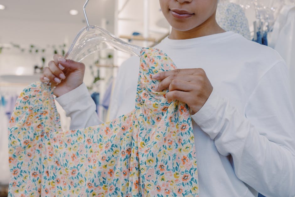 Close-up of a woman holding a floral dress on a hanger inside a boutique store.