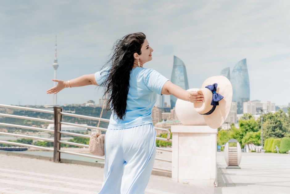 An adult woman embraces the view of Flame Towers in Baku, Azerbaijan, on a sunny day.