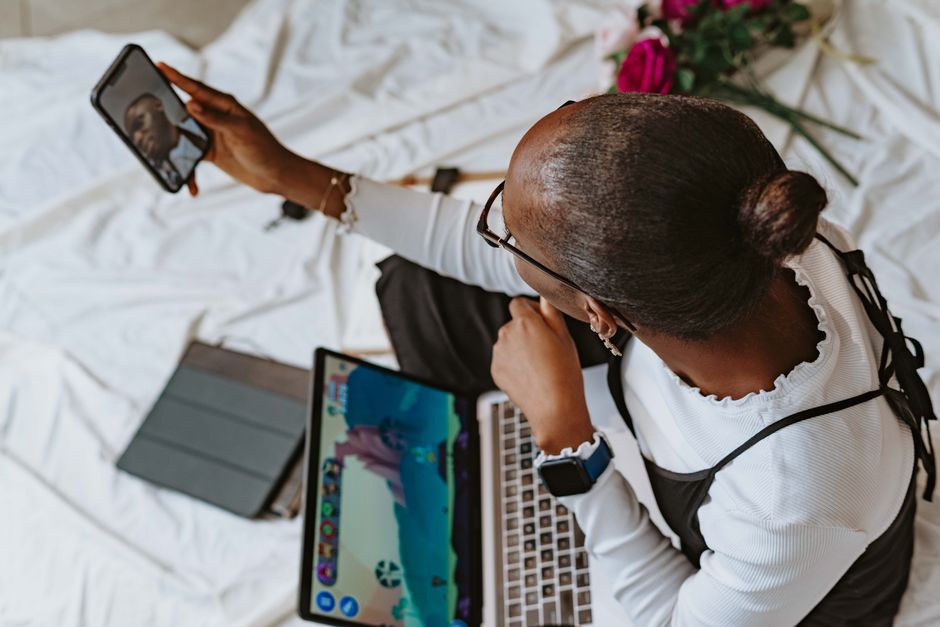A woman in Abuja, Nigeria, multitasking with smartphone and laptop during remote work.