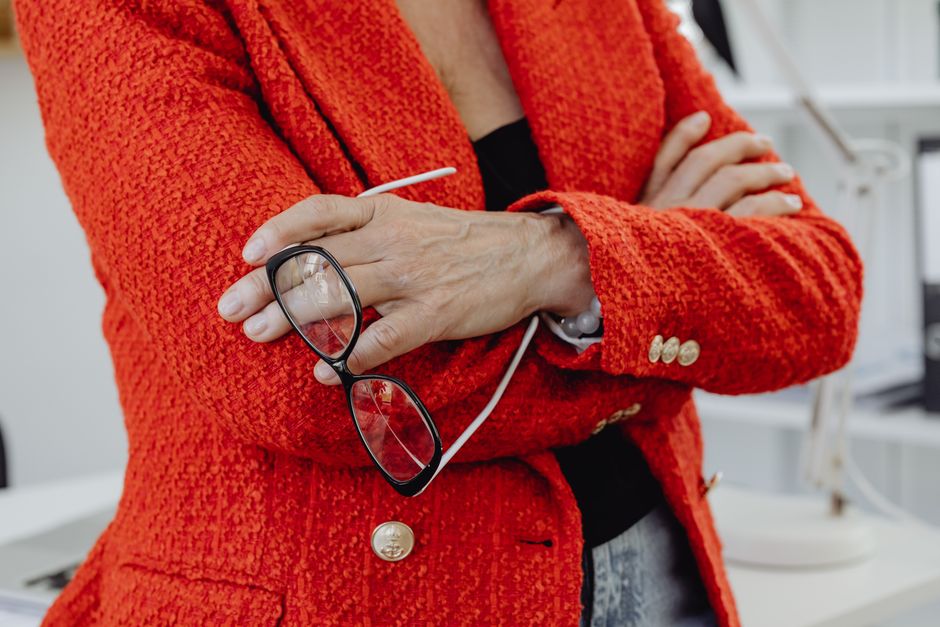 Close-up of a businesswoman in a red blazer holding eyeglasses, embodying confidence.