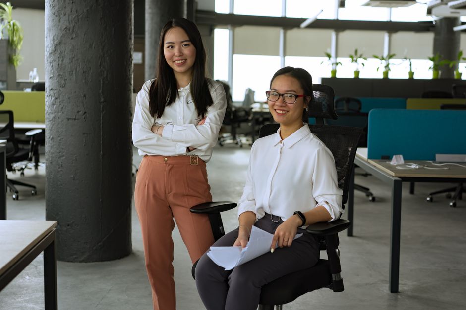 Two women in a contemporary office, smiling and interacting, promoting teamwork and collaboration.