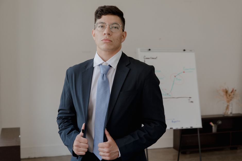 A well-dressed businessman in a suit stands confidently in front of a flip chart in an office.