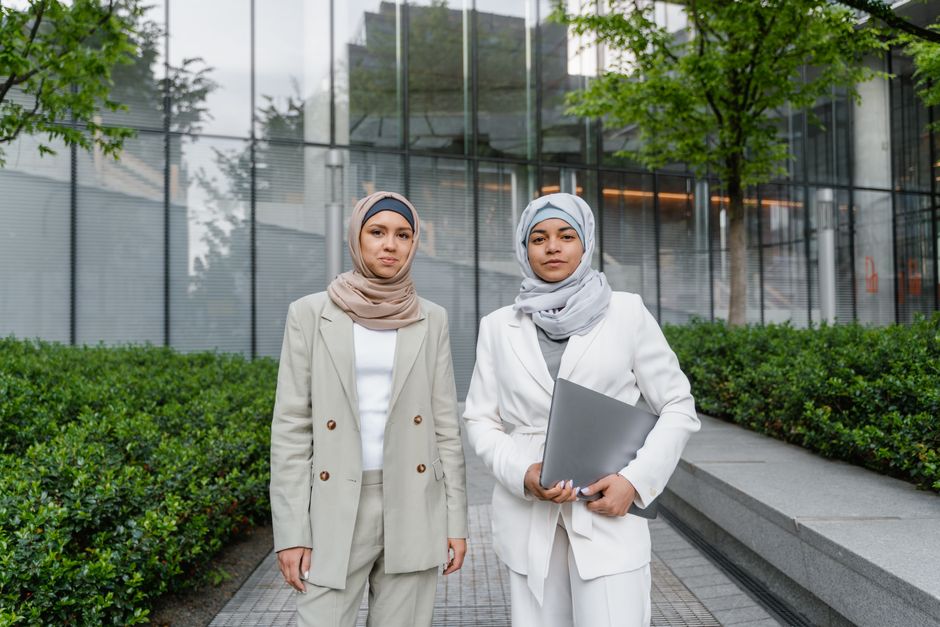 Two confident businesswomen in hijabs and formal wear standing outdoors in an urban setting.