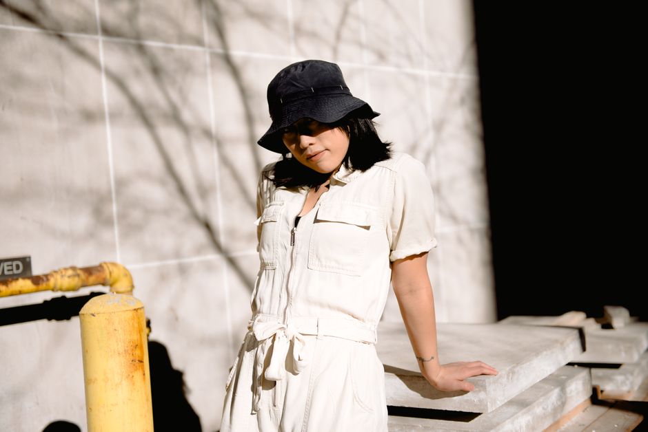 Young female wearing casual wear standing near cement board and covering eyes from sunlight with hat