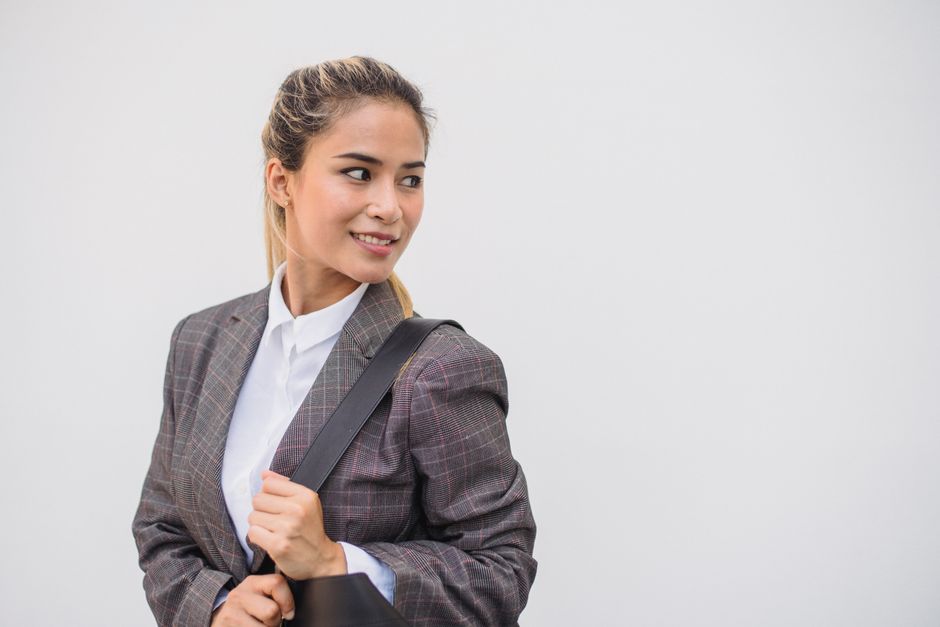 Confident woman in plaid blazer with a bag, looking back against a white background.