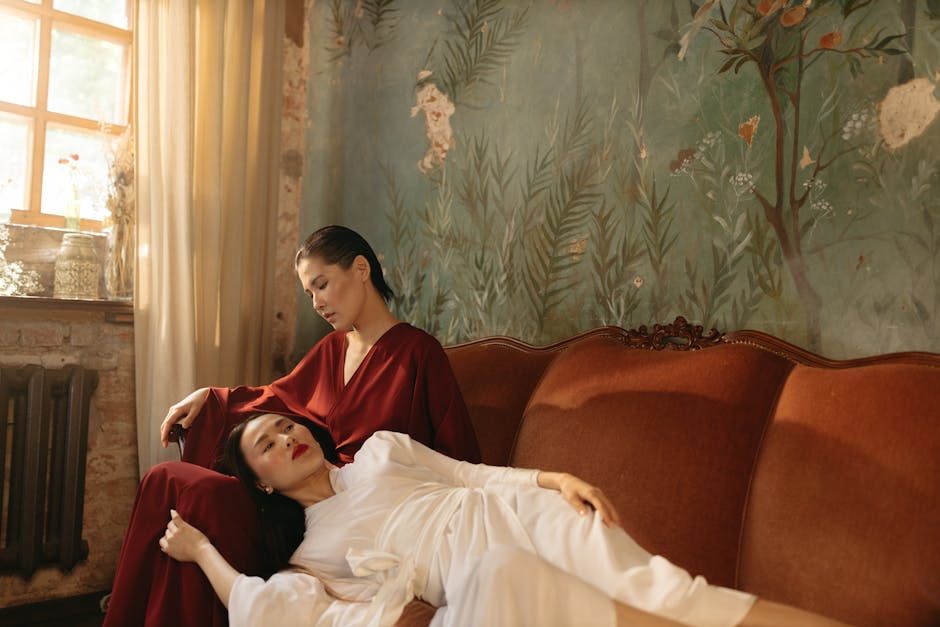 Two women share a tranquil moment on a vintage sofa in a cozy, softly lit room.
