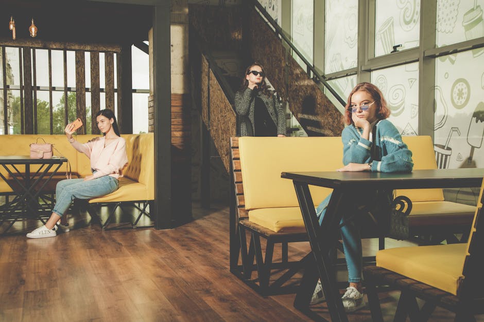 Three fashionable women posing in trendy indoor cafe setting, showcasing modern style.