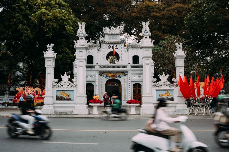 Dynamic scene of Quán Thánh Temple in Hanoi with passing motorbikes, showcasing vibrant culture.