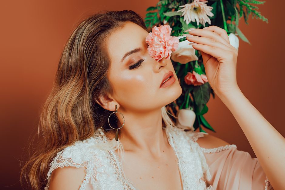 Stylish woman holding flowers with a red backdrop, exuding elegance and beauty.
