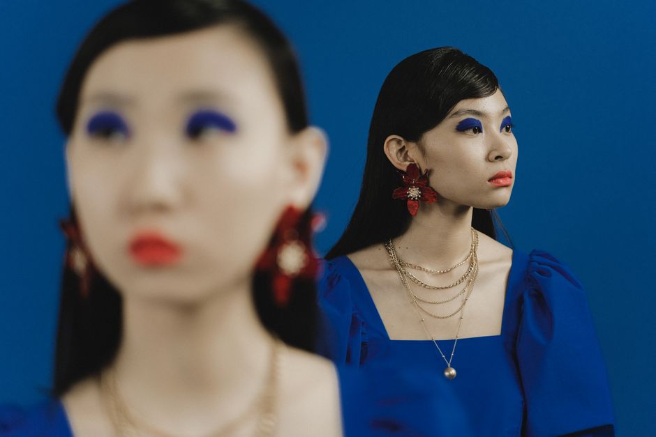 Stylish Asian women in blue dresses with bold makeup and jewelry against a blue background.