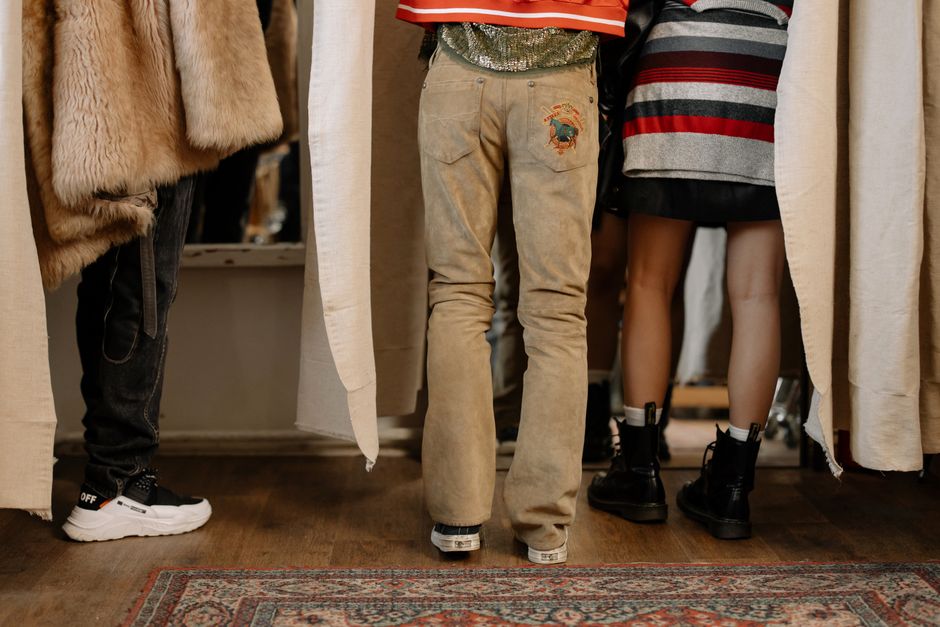 Rear view of casually dressed individuals standing indoors on a wooden floor and carpet.