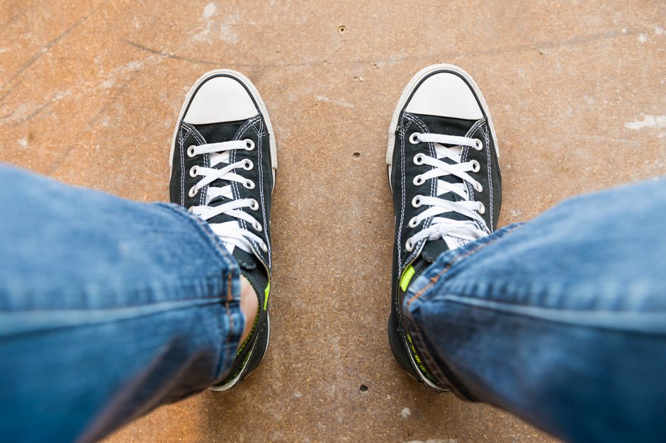 Pair of black sneakers with white shoelaces on a stone surface, captured from above.