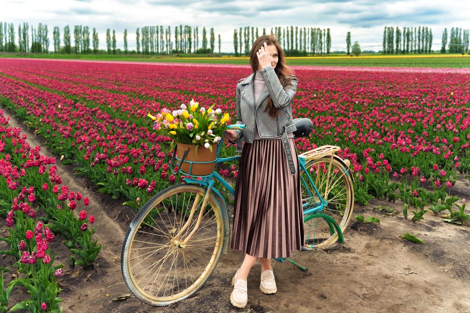 Young woman with retro bicycle and tulips in a colorful flower field, symbolizing spring and leisure.