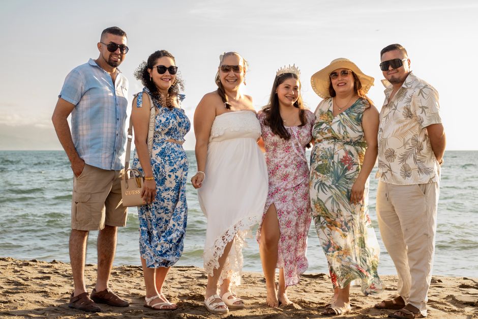 Group photo of a happy family enjoying a sunny day at the beach with smiles and colorful attire.