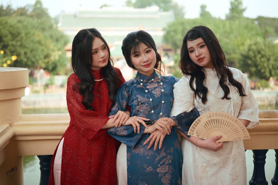 Three women in elegant Ao Dai dresses pose gracefully in a serene outdoor setting.