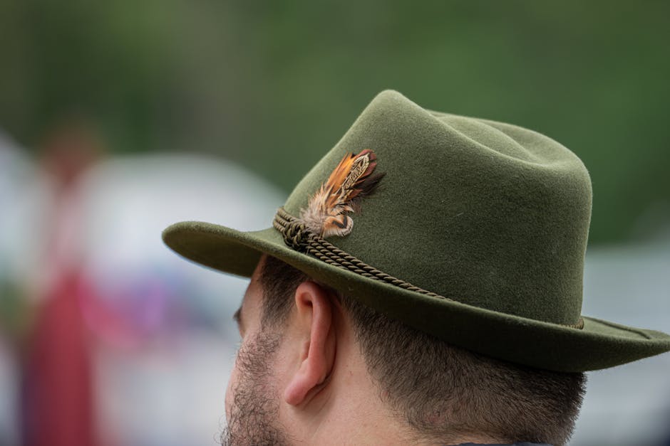 Profile view of a man wearing a green hat with a feather, outdoors.
